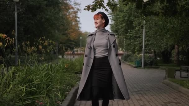 Young attractive redhead short-haired girl in a black beret and gray coat in a natural park on an autumn day. — Stock Video