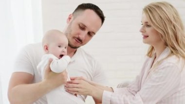 Beyaz bir yatakta yeni doğmuş bir bebeği olan, beyaz, sevecen bir beyaz aile. Ev kıyafetleri ve rahat bir atmosfer..