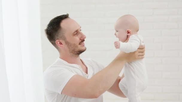 Bebê recém-nascido caucasiano em roupas brancas nos braços de um jovem pai amoroso. — Vídeo de Stock