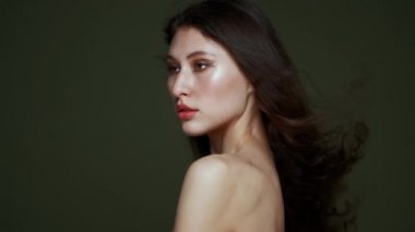 Uzun kıvırcık siyah saçlı, göğüs portresi, çıplak omuzlu güzel bir genç kadın. Güzel doğal ten. Kırmızı dudaklar ve zarif eller. Kız stüdyoda zeytin arkaplanda poz veriyor.