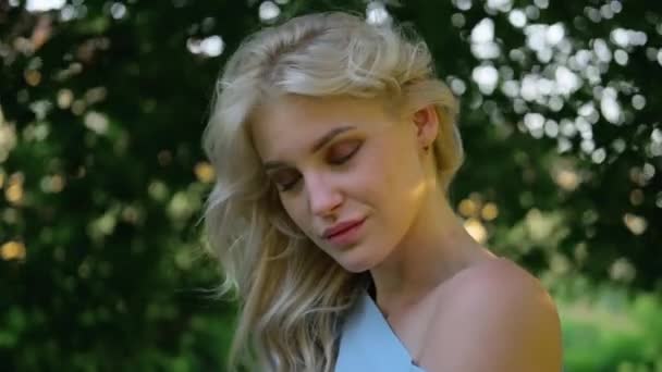 Portret młodej, pięknej dziewczyny 21 lat w niebieskiej sukience letniej. Kobieta się uśmiecha. Piękne usta i oczy. Długie kręcone blond włosy. — Wideo stockowe