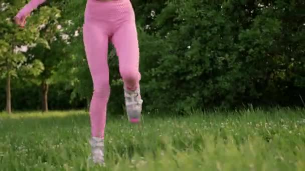 Eine junge, schlanke, schöne Frau mit Dreadlocks in Sportkleidung trainiert draußen im Park. Kangoo springt beim Training. — Stockvideo