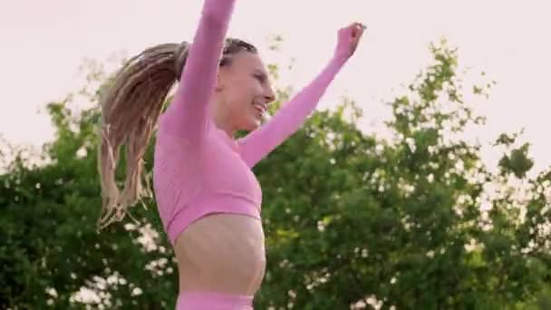 Una joven esbelta mujer hermosa con rastas en trenes de ropa deportiva en el parque al aire libre. Kangoo salta de entrenamiento. — Vídeos de Stock