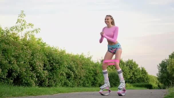 Mladá štíhlá krásná žena s dredy ve sportovním oblečení vlaky v parku venku. Kangoo skokový výcvik. — Stock video