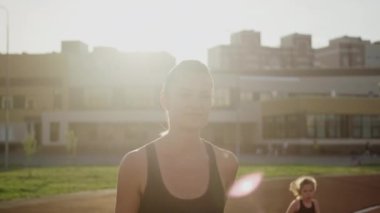 Spor giyimli güzel bir kadın stadyumun koşu bandında koşuyor. Gün batımında koşu, yaz akşamı..