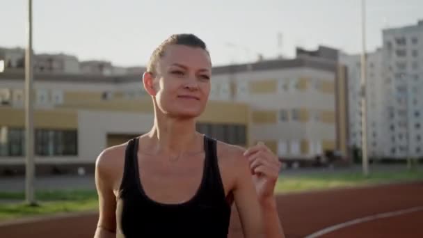 En vacker ung kvinna i sportkläder springer på löpbandet på arenan. Jogga vid solnedgången, sommarkväll. — Stockvideo