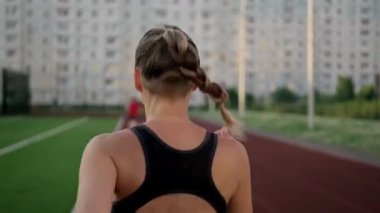 Spor giyimli güzel bir kadın stadyumun koşu bandında koşuyor. Gün batımında koşu, yaz akşamı..