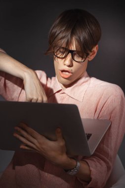 Bu bilgisayar nerd. Yaratıcı genç millenial portre kapalı. Mutlu yüz ifadesi içinde gözlük ile komik genç adam sarılmak dizüstü karanlık bir arka plana dayanır. Internet, video oyun bağımlılık kavramı