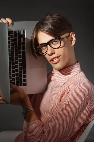 Computernerd. kreatives Teenie-Millenial-Porträt drinnen. Lustiger junger Mann mit glücklichem Gesichtsausdruck in Brille umarmt Laptop vor dunklem Hintergrund. Internet, Videospielsucht — Stockfoto