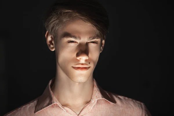 Close-up portrait of Caucasian attractive young man blinked his eyes. light shines from below. Standing Isolated on black background and looking at camera. Fear concept — Stock Photo, Image