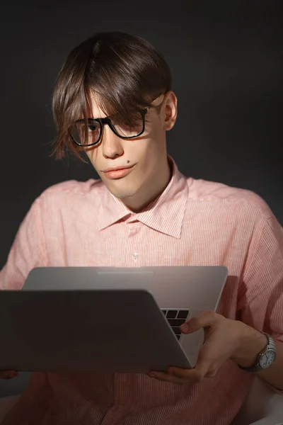 IT computer nerd. Creative teen millenial portrait indoors. Funny young man with happy face expression in glasses hug laptop against dark background. Internet, video game addiction concept