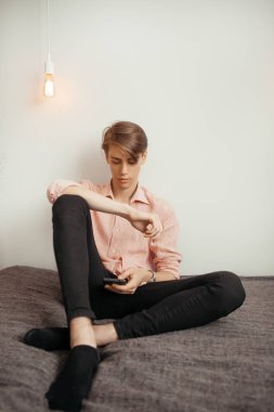 Çizgili gömlek ve siyah kot pantolon genç bir çekici adam kapalı bir akıllı telefon okuma veya film izlerken, ya online ya da çevrimdışı oturuyor. Öğrenme, boş zaman, uzaktan çalışma kavramı