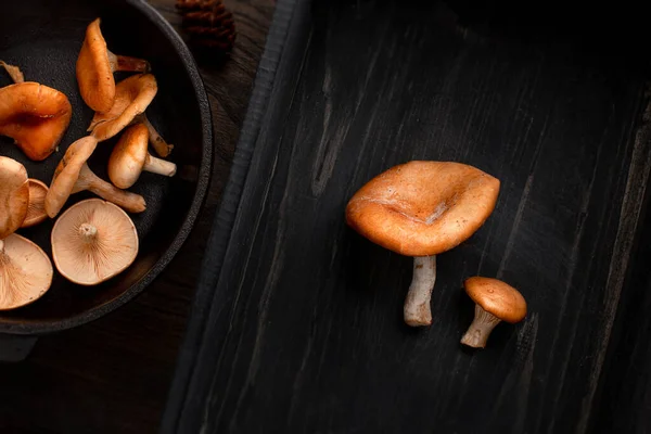 Raw färsk svamp på gjutjärn pan vänster, och två svampar på höger sida, på trä bakgrund. Ovanifrån, utrymme för text — Stockfoto