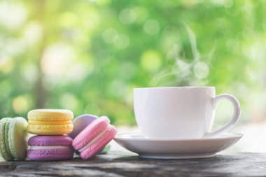 Arka planda doğa bahçesinin üzerinde sıcak kahve fincanı olan renkli kurabiyeler.