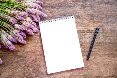 Güzel pembe çiçek, boş kağıt not defteri ve tahta masadaki kalem.