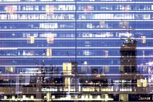 City office life. office workers light up the multiple floors office building and work overtime in the night time. glasses steel and aluminum clad modern office in Bangkok business district.