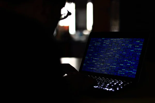 电脑黑客剪影在电脑上打字在一个黑暗的房间 使用蓝色二进制代码技术 二进制数据 计算机编程和网络安全概念 — 图库照片