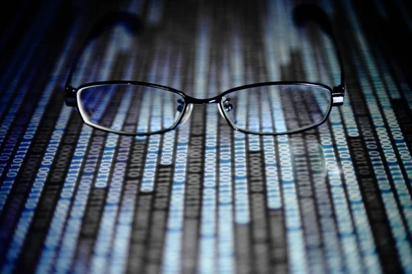 big data analysis. blue binary code on led panel with black background and glasses placed over the information panel. hacker and source code analysis.