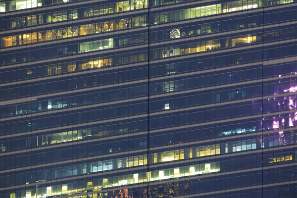 multi-storey office building at night with worker working overtime. late night at office. lighting and working people within. Late night overtime in aglasses steel and aluminum clad modern office