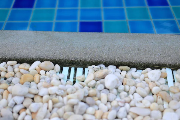 swimming pool drainage system grating covered with round white river stone pebble. swimming pool architectural detail design. White pebble contrasting with dark grey aggregate stone pool edge