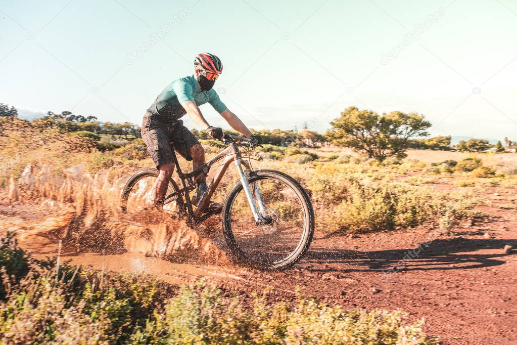 mountain biker wearing a protective cloth face mask riding through a muddy puddle