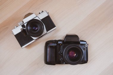 Açık ahşap arka planda iki adet 35 mm 'lik eski film kamerası.