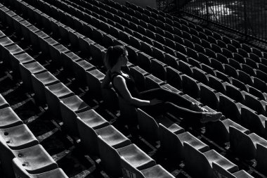 Genç güzel sarışın Spor Stadyumu tribünü üzerinde oturan kız. tek renkli