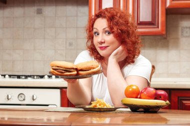 Büyük kadın yemek lokanta. Kızıl saçlı şişman kız burger, patates ve meyve ile. Sağlıksız yiyecek konsepti ile artı boyutu kadın mutfak