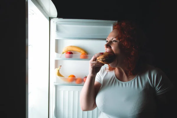 Büyük kadın yemek lokanta. Kızıl saçlı şişman kız buzdolabı içinde burger ile arıyorum. Sağlıksız ve sağlıklı gıda kavramı ile artı boyutu kadın mutfak