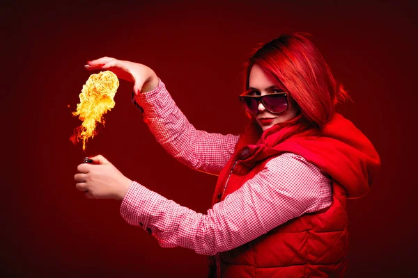 Red hair girl in studio with red color clothes, close portrait with cigarette lighter in hand and big fire