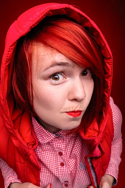 Kızıl saçlı kız Studio kırmızı renk giysileri ile yakın dikey, sürpriz ve dalgın yüz