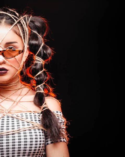 Portrait of cool crazy brunette fashionable girl in glasses, casual hairdo. Woman tied up with a rope, with beauty makeup and clock. Time loop, isolated lady with red glowing black background