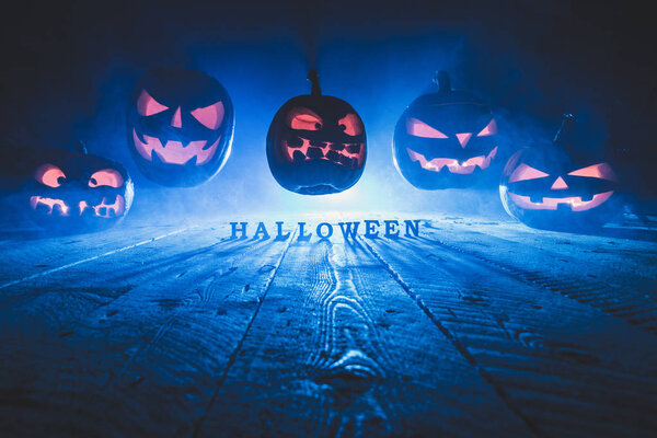 Concept of Halloween. Many glowing fiery light of evil scary pumpkins flying through the air. jack lantern, with the inscription Halloween, with blue cool light behind on wooden background