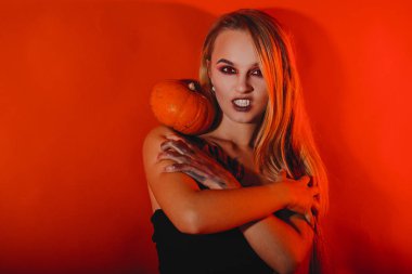 Cadılar Bayramı kız vampir kırmızı gözleri kırmızı dudakları ve koyu kırmızı arka plan ile. Korkunç kadın oyun ya da şeker zamanı, Cadılar Bayramı kavramı. Elinde kabak ile tatil için kadın makyaj 