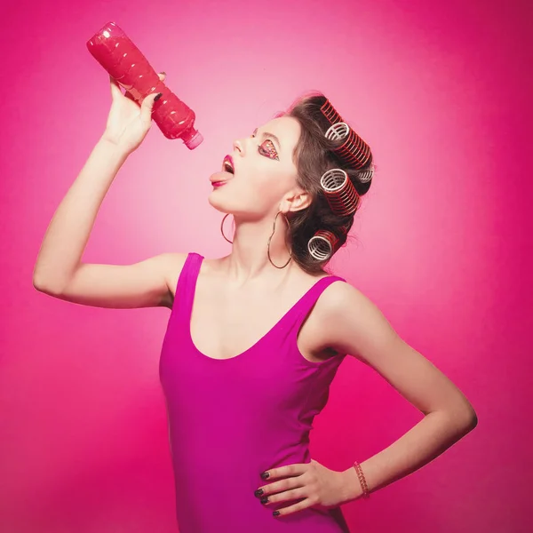 Chica descarada con botella y agua rosa posando sobre fondo rosa —  Fotos de Stock