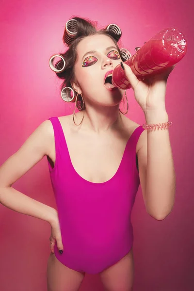 Freche Mädchen mit Flasche und rosa Wasser posiert auf rosa Hintergrund — Stockfoto