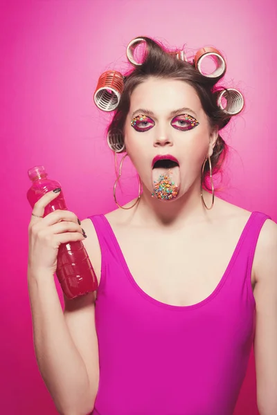 Freche Mädchen mit Flasche und rosa Wasser und Süßigkeiten auf der Zunge posi — Stockfoto