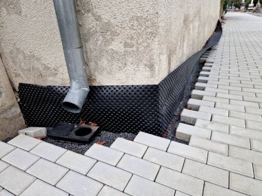 The perimeter of the house foundation is separated from the sidewalk by black bubble wrap. It protects the house from moisture. The sidewalk bricks are not finished. The trims are missing.trim