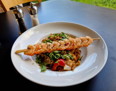Shrimp skewer on with fried rice and teriyaki sauce. in a plate on the table with salt and pepper shakers