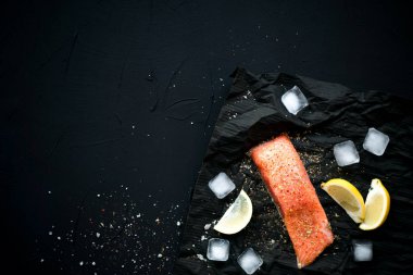 Buz ve limon ile siyah arka plan üzerine baharat ile taze somon. Kuş bakışı. Sağlıklı ve diyet kavramı.