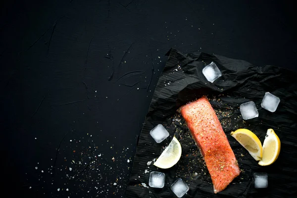 Buz ve limon ile siyah arka plan üzerine baharat ile taze somon. Kuş bakışı. Sağlıklı ve diyet kavramı.