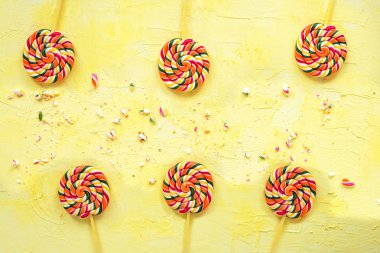 Sarı arka planda sopa üzerinde çok renkli lolipoplar. Üst te. Doğum günü için şenlikli veya doğum günü arka plan. Gökkuşağı lolipop.