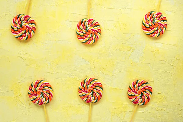 Multicolored lollipops on stick on yellow background.Top view.Festive or birthday background for birthday.Rainbow lollipops.