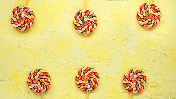 Multicolored lollipops on stick on yellow background.Top view.Festive or birthday background for birthday.Rainbow lollipops.