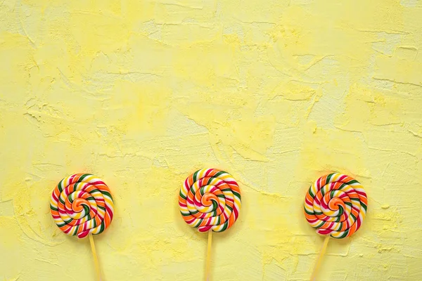 Multicolored lollipops on stick on yellow background.Top view.Festive or birthday background for birthday.Rainbow lollipops.