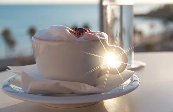 White cup of coffee and glass of water on sea beach and palms  At Sunset Or Sunrise Beach, holiday concept