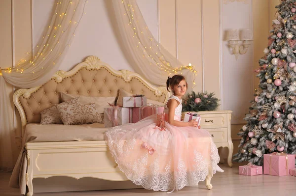 バラのドレスの少女はベッドの上のクリスマスの贈り物に目が覚めた — ストック写真
