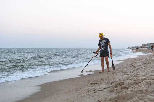 Treasure hunter with a metal detector walks along the beach of the Black Sea after sunset looking for treasure