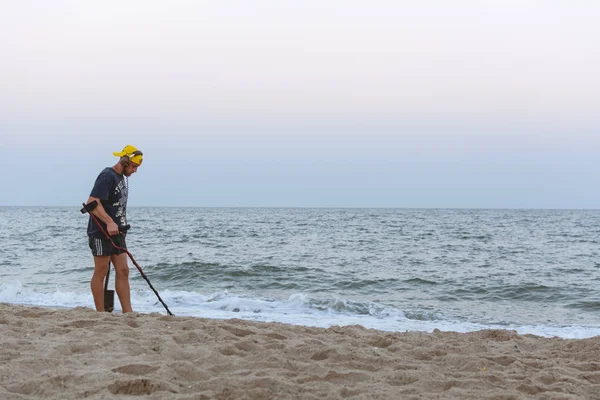 Treasure hunter with a metal detector walks along the beach of the Black Sea after sunset looking for treasure