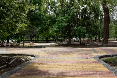 Parkta renkli beton döşeme döşemeleri. Profesyonel işçiler yeni kiremitler dikiyor ve seviyelendirilmiş kum temeline kaldırım döşemesi döşüyor..